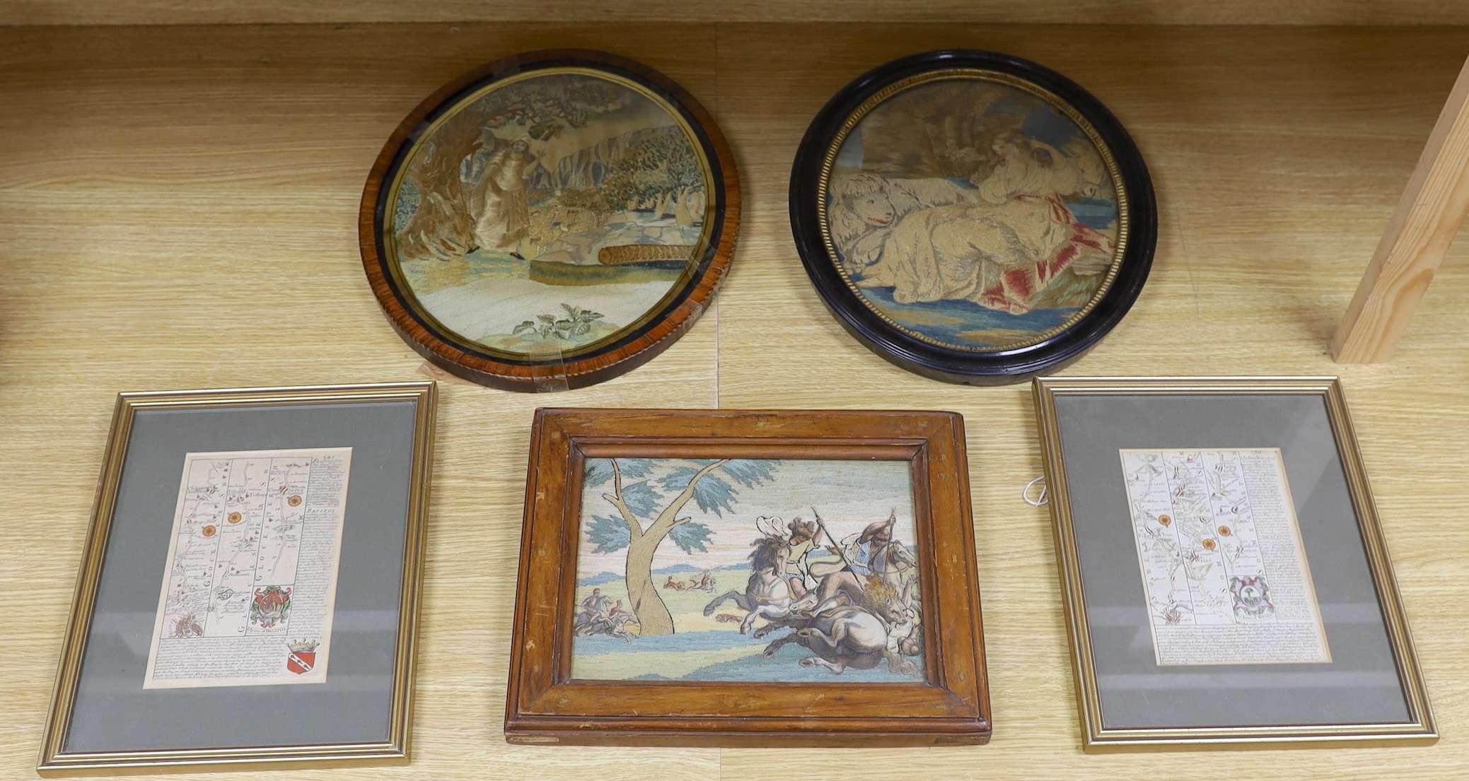 Three late 19th / early 20th century framed tapestries - a mountain scape with farmer and heard, a female figure with animal, and a with lions and men on horseback fighting scene, together with two maps - ‘Gloucestershir